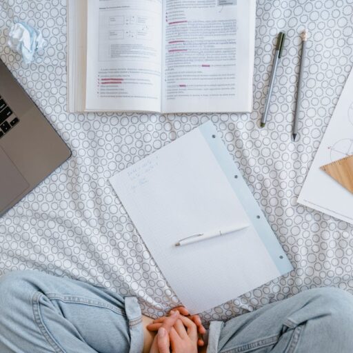 Flat lay of a study area with an open laptop, books, notes, and stationery on a bed.